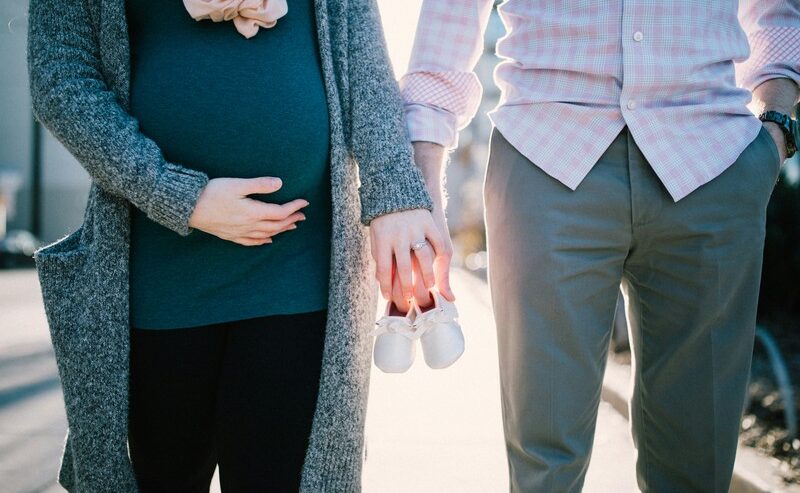 Man With Pregnant Woman Holding Baby Shoes In Daylight